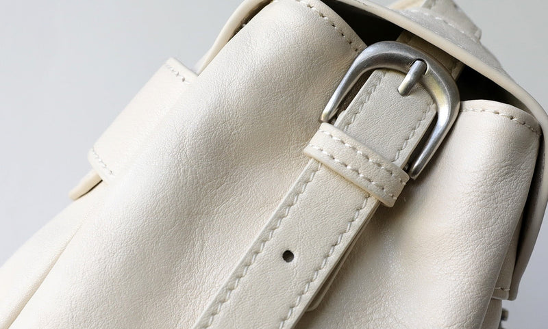 Close-up of a white leather bag with a silver buckle on a light gray background