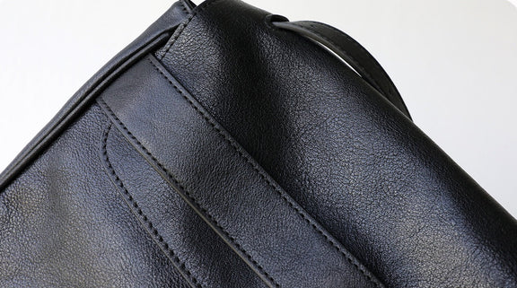 Close-up of a black leather bag with visible stitching on a light gray background