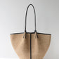 Beige woven handbag with black handles and trim on a light gray background