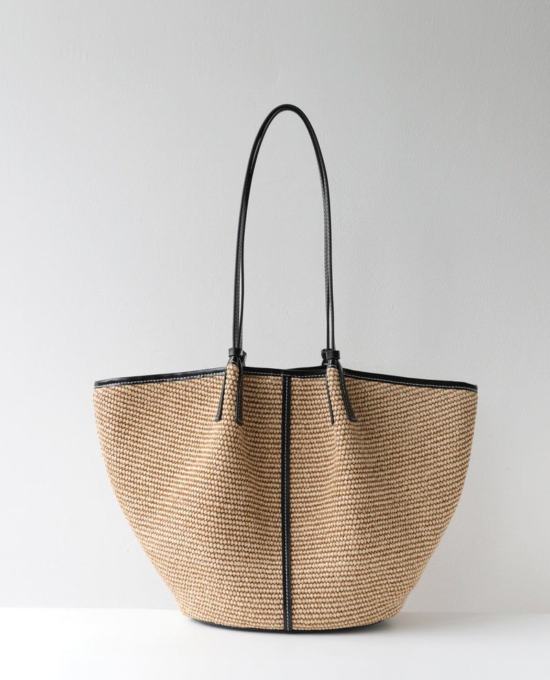Beige woven handbag with black handles and trim on a light gray background