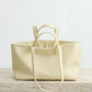 Cream-colored leather tote bag on a light wooden surface with a white background
