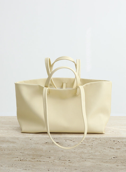 Cream-colored leather tote bag on a light wooden surface with a white background