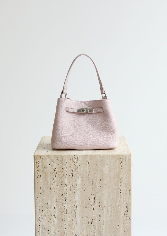 Pink handbag on a wooden block with 'Shevennie Studio' branding.