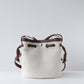 White bucket bag with brown leather straps on a light gray background