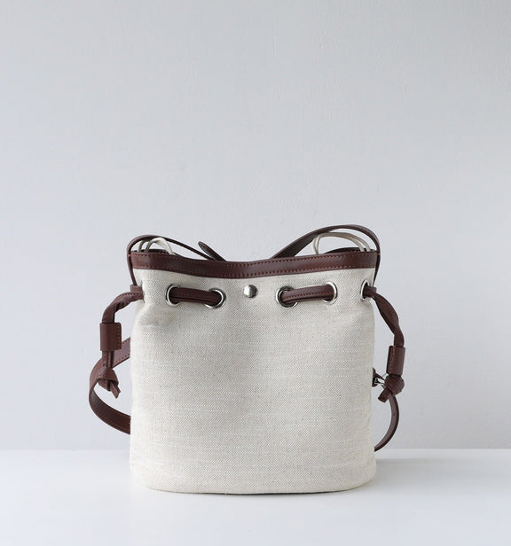 White bucket bag with brown leather straps on a light gray background