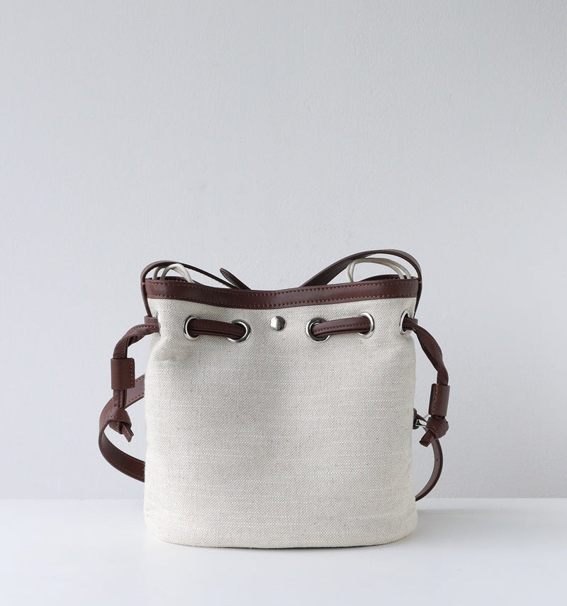 White bucket bag with brown leather straps on a light gray background