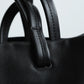 Close-up of a black leather handbag with handles.