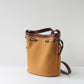 Yellow bucket bag with brown leather straps on a light gray background