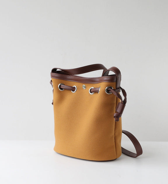 Yellow bucket bag with brown leather straps on a light gray background