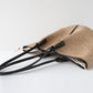 Beige straw handbag with black straps on a white background