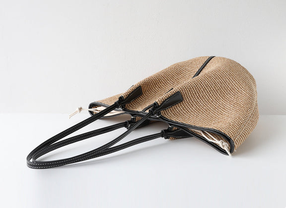 Beige straw handbag with black straps on a white background