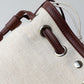 Close-up of a beige bag with brown leather straps and hardware on a gray background