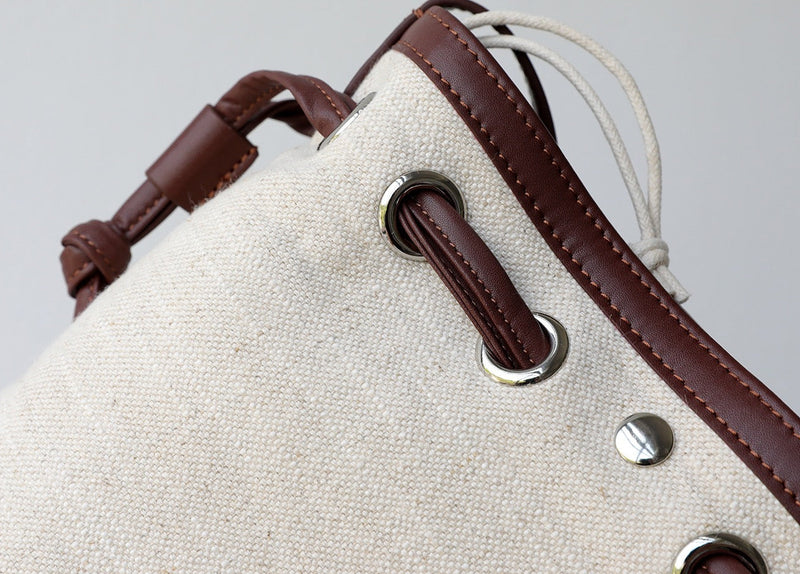 Close-up of a beige bag with brown leather straps and hardware on a gray background