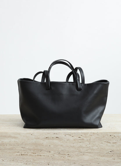 Black leather handbag on a light wooden surface with a white background