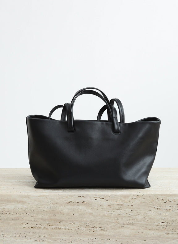 Black leather handbag on a light wooden surface with a white background