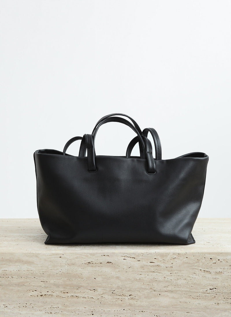 Black leather handbag on a light wooden surface with a white background
