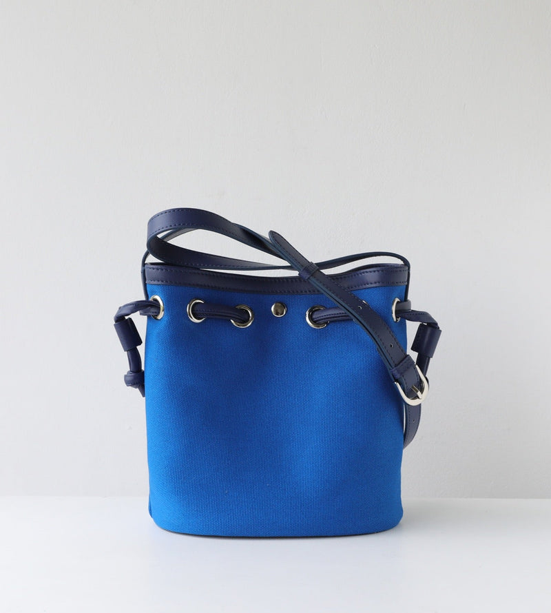 Blue bucket bag with black leather straps on a light gray background