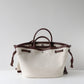 White tote bag with brown leather handles and accents on a light gray background