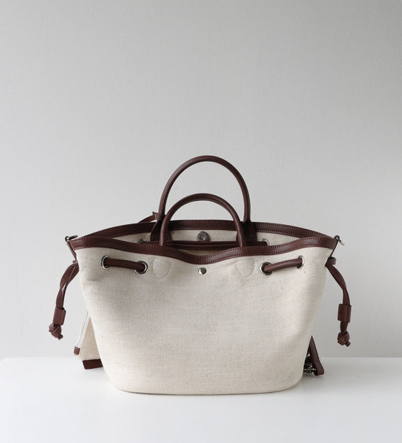 White tote bag with brown leather handles and accents on a light gray background