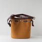 Brown leather bucket bag with brown strap on a light gray background
