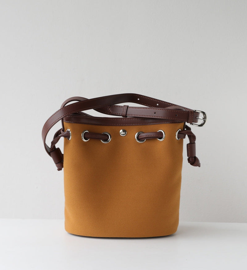 Brown leather bucket bag with brown strap on a light gray background