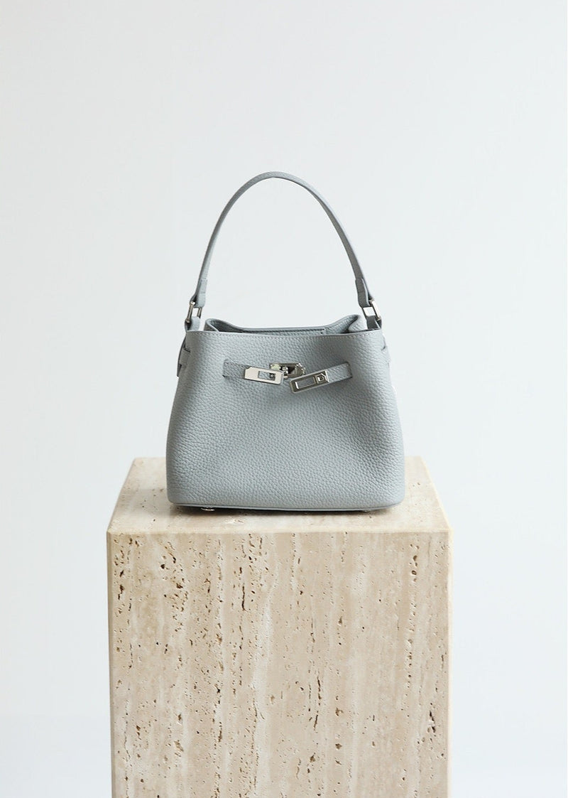Gray handbag on a wooden block with 'Shevennie Studio' branding.