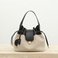 A beige canvas bucket bag with black leather trim, dual top handles, and drawstring details, displayed on a light stone surface against a white background with 'Shevennie Studio' text at the top.