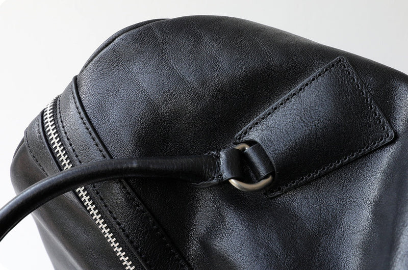 Close-up of a black leather bag with a zipper detail on a light gray background