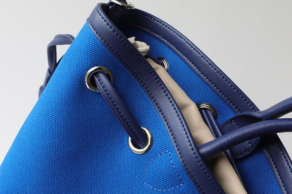 Blue handbag with drawstring closure on a light gray background