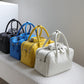 Five handbags in black, blue, yellow, and white on a white surface with a gray background.