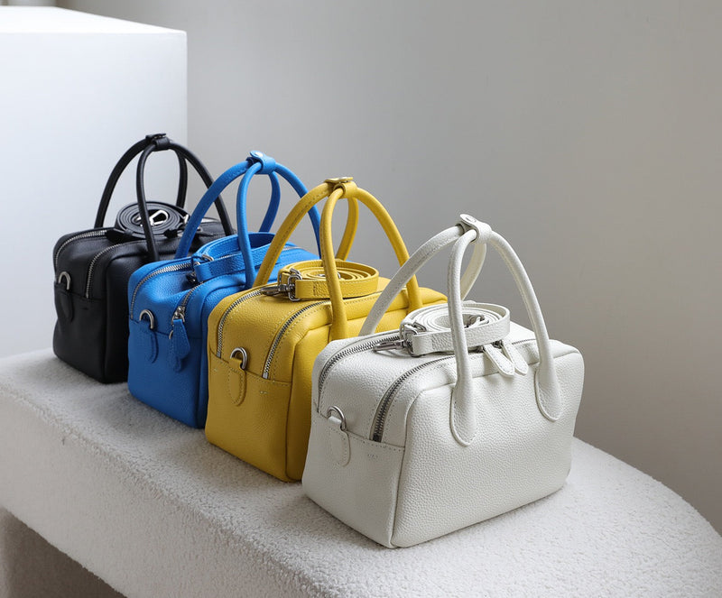 Five handbags in black, blue, yellow, and white on a white surface with a gray background.