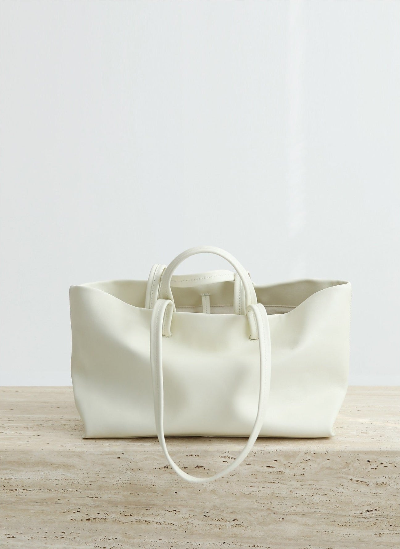 White leather tote bag on a wooden surface with a light gray background