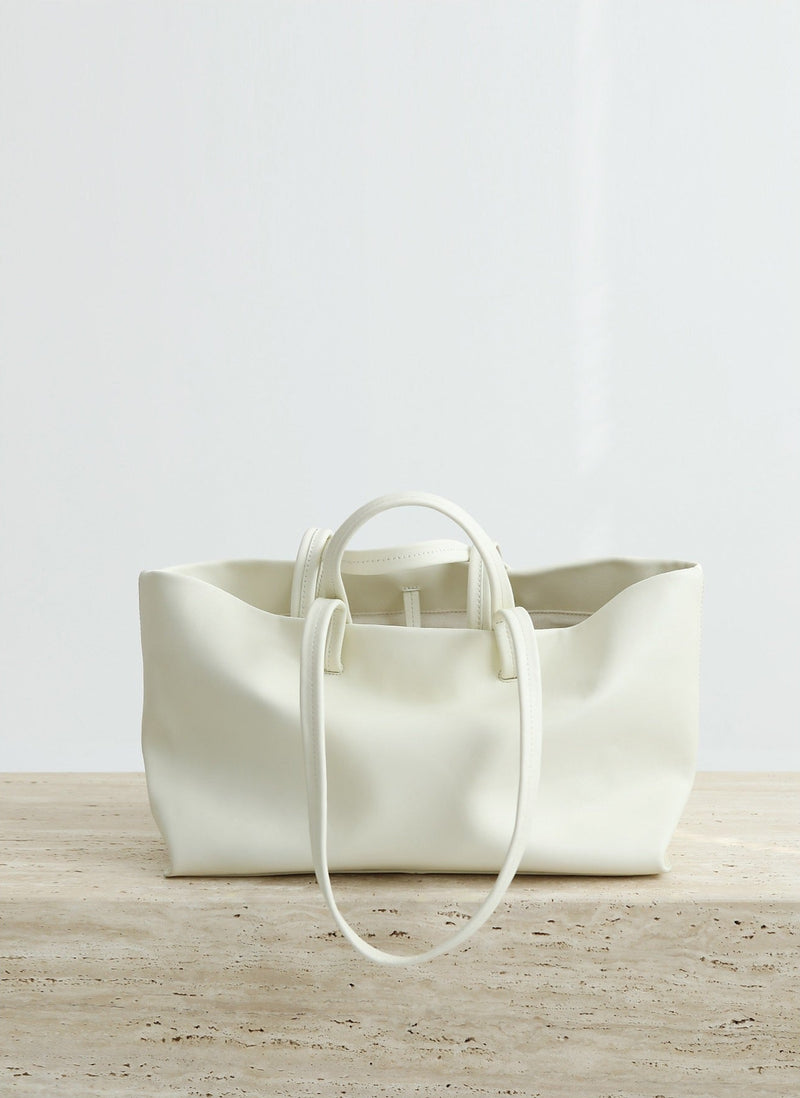 White leather tote bag on a wooden surface with a light gray background