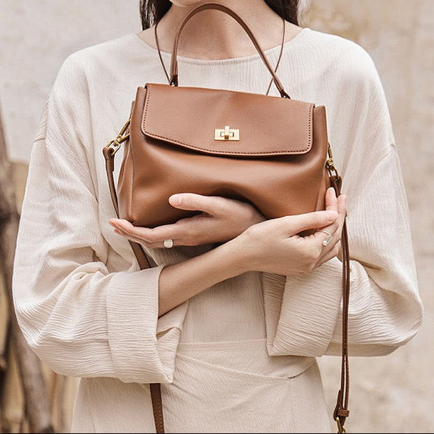 Woman holding a brown leather handbag against a neutral background