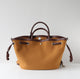 Brown leather handbag with matching handles and drawstring on a light gray background