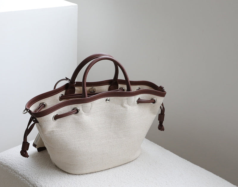 White tote bag with brown handles and accents on a light surface.