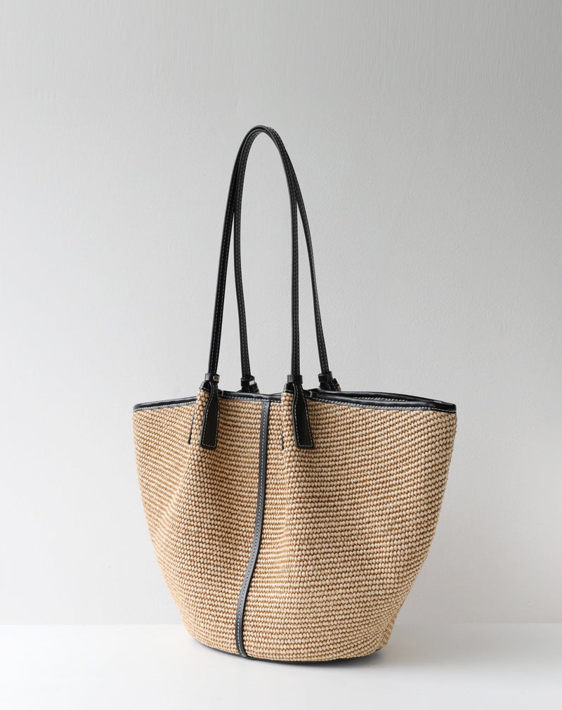 Woven handbag with black straps on a light gray background