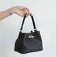 Black handbag held by a hand on a white background