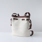 Beige bucket bag with brown leather straps on a light gray background