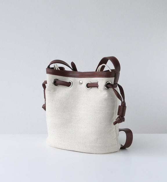 Beige bucket bag with brown leather straps on a light gray background