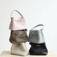 Five handbags in different colors stacked on a wooden surface with a light gray background