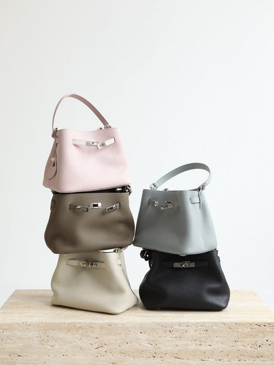 Five handbags in different colors stacked on a wooden surface with a light gray background
