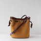 Brown leather bucket bag with a strap on a light gray background