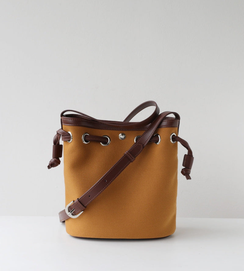 Brown leather bucket bag with a strap on a light gray background