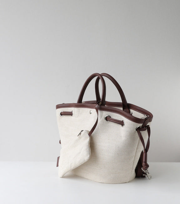 Canvas handbag with brown leather handles and accents on a light gray background