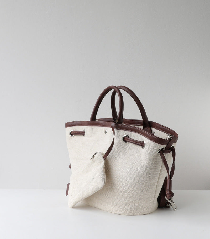 Canvas handbag with brown leather handles and accents on a light gray background