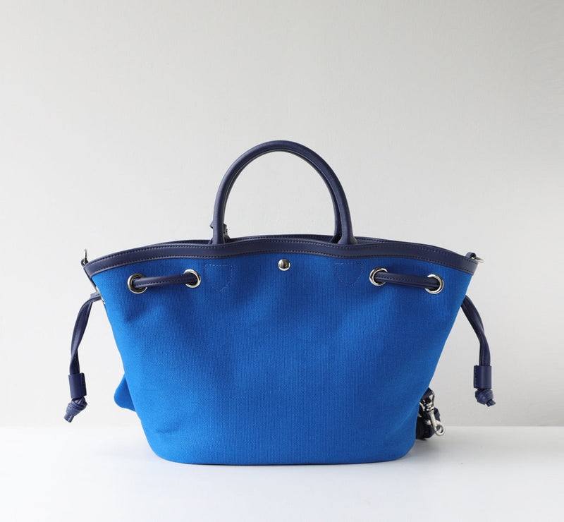 Blue tote bag with black handles and drawstring on a white background