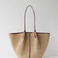 Woven handbag with brown handle and trim on a light gray background