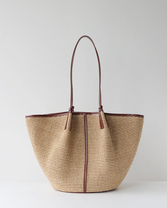 Woven handbag with brown handle and trim on a light gray background