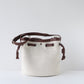 White bucket bag with brown leather straps on a light gray background